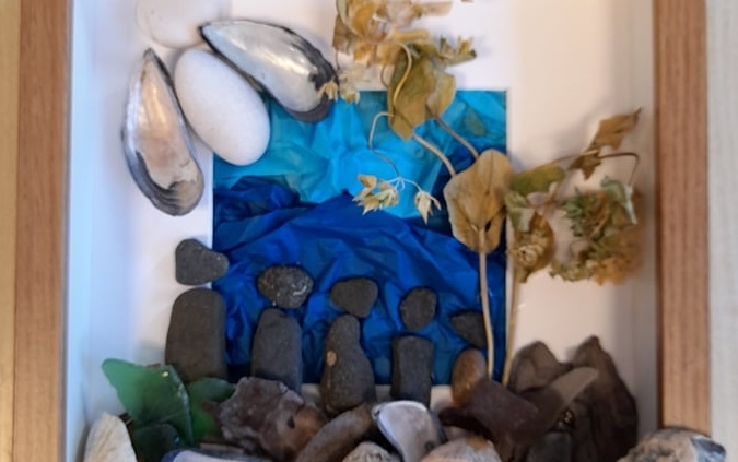 Box frame using stones and shells to create a representation of a family.